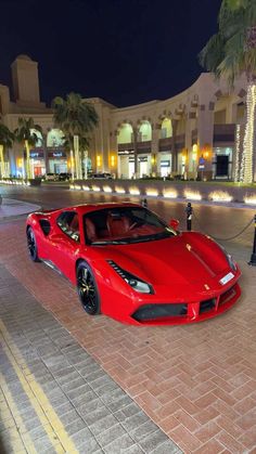 a red sports car parked in front of a shopping center at night with palm trees