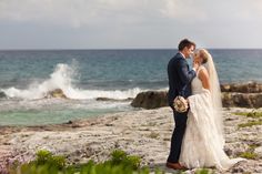 a bride and groom are standing on the rocks by the ocean looking at each other