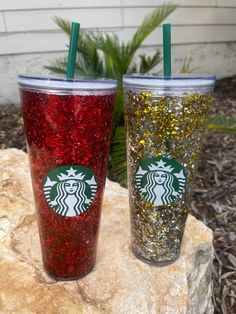 two starbucks cups sitting on top of a rock next to each other with straws in them