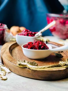 two bowls filled with cranberry sauce sit on a wooden tray next to other dishes