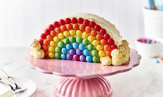 a rainbow cake on a pink plate with white frosting and sprinkles