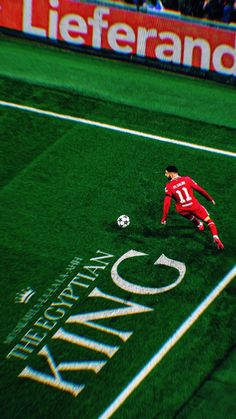 a soccer player in red kicks the ball on green field with white line and lettering