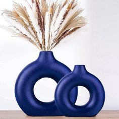 two blue vases sitting on top of a wooden table next to dry grass and feathers