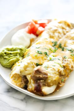 an enchilada on a white plate with guacamole and tomatoes