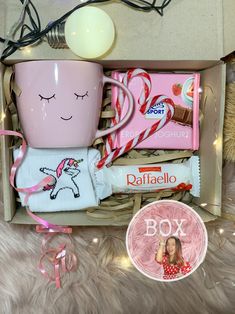 a pink coffee mug sitting inside of a box next to some candy and candies