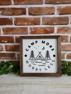 a wooden frame with the words camp more worry less on it next to a brick wall