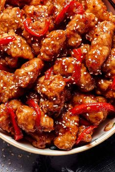 a bowl filled with chicken and peppers covered in sesame seed flakes on top of a table