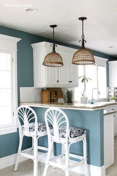 two white bar stools sitting in front of an island with three lights hanging over it