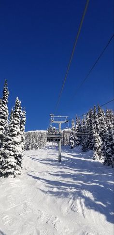 a ski lift going up the side of a snow covered slope with trees on both sides