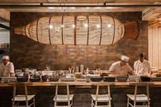 two chefs in a kitchen preparing food behind the counter with chairs and lights hanging from the ceiling