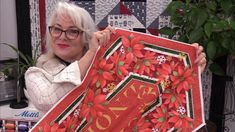 a woman holding up a red and green christmas quilt with poinsettis on it