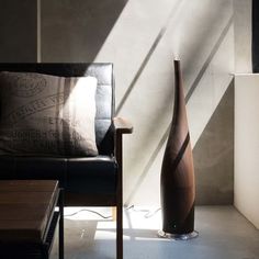 a large vase sitting next to a black chair in a room with sunlight coming through the window