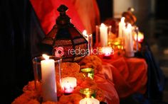 many candles are lit on a table with orange flowers and red cloth draped around it