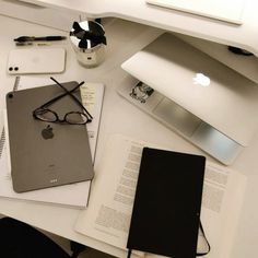 an apple computer sitting on top of a white desk next to a book and glasses