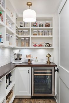 a kitchen with white cabinets and wood flooring is pictured in this image, there are shelves that have wine bottles on them