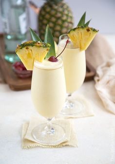 two glasses filled with drinks sitting on top of a white table next to a pineapple