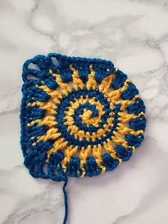 a blue and yellow crocheted doily on a white marble countertop with a string attached to it