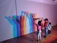 three children are standing in front of a colorful wall with their hands up to the ceiling