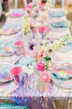 the table is set with pink and purple flowers in vases, plates, cups, and napkins