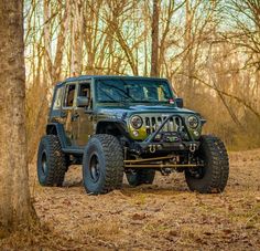 a green jeep parked in the middle of a wooded area with trees and leaves on the ground