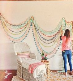 a woman standing next to a bed in a room with wooden floors and walls decorated with multicolored garlands