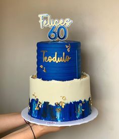 a blue and white cake with the number 60 on top is being held by a woman