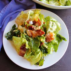 a salad with bacon and lettuce is on a white plate next to a blue napkin