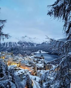 an aerial view of a town in the mountains with snow on them and trees around it