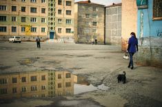 a woman walking her dog in the middle of an empty parking lot next to buildings