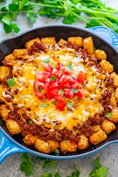 a skillet filled with tater tots covered in cheese and tomatoes, garnished with cilantro