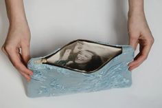 two hands holding a blue purse with an image of a woman and man on it