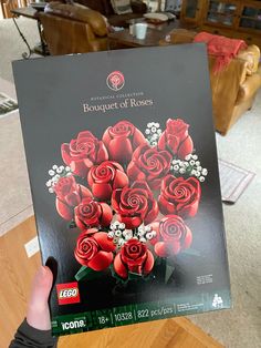 a person holding up a box with roses on it in front of a couch and coffee table