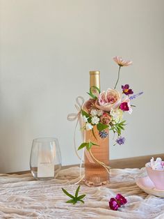 a table topped with a vase filled with flowers and a bottle of wine next to it