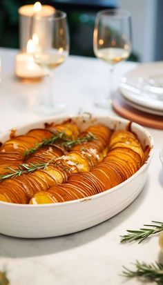 a white dish filled with potatoes on top of a table next to glasses and plates