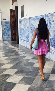 a woman in a pink dress is walking down the hall with a blue and white tile wall behind her