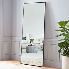 a large mirror sitting on top of a wooden floor next to a potted plant