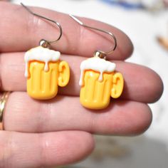 a pair of yellow and white earrings with beer mugs on them in the palm of someone's hand