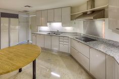 an empty kitchen with white cabinets and marble counter tops, along with a wooden dining table