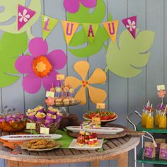 a table topped with lots of food next to a wall covered in green and pink flowers