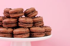 a white cake plate filled with chocolate macaroons on top of a pink background