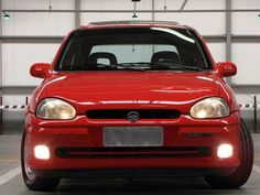 a red car parked in a garage with its lights on and the front bumper up