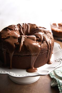 a chocolate bundt cake on a white plate topped with frosting and drizzled