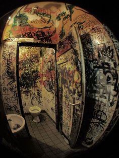 a public bathroom with graffiti all over the walls and floor, along with urinals