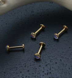 three small gold colored studs on a blue surface with water droplets around them and a bone in the background