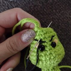 a person holding a green crocheted object with needles in their hand and the needle sticking out of it