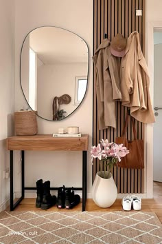 there is a coat rack in the entryway with shoes on the floor and a mirror above it