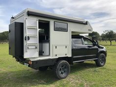 an off road truck with a camper attached to the back in a grassy field