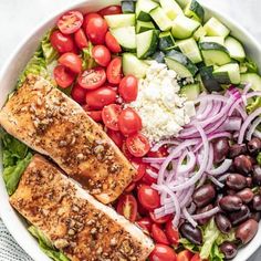 a salad with salmon, tomatoes, cucumber, olives and feta cheese