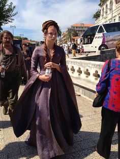 a woman in a purple dress is walking down the street with other people behind her