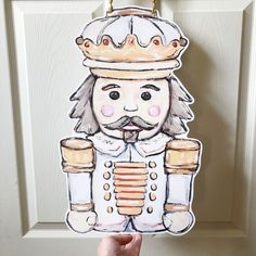 a hand holding up a paper cutout of a nutcracker wearing a crown